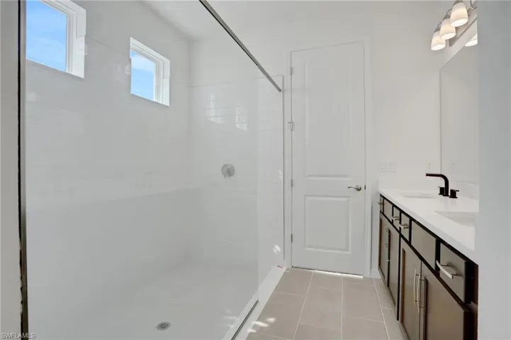 Bathroom featuring walk in shower, double vanity, and light tile patterned floors