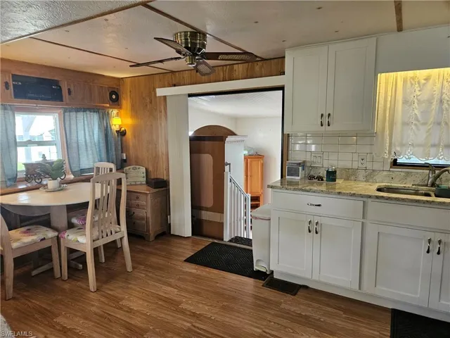 Kitchen featuring a sink, wood finished floors, backsplash, white cabinets, and ceiling fan