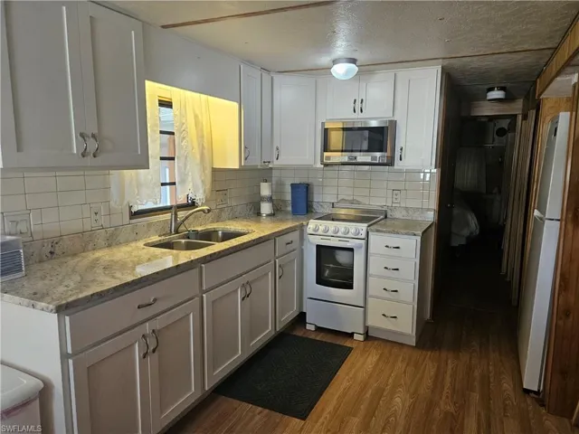 Kitchen with stainless steel microwave, range, freestanding refrigerator, dark wood finished floors, and tasteful backsplash