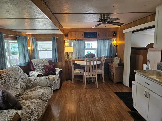 Living room with a ceiling fan, wooden walls, and wood finished floors
