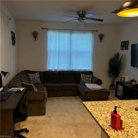 Living area with carpet flooring, a ceiling fan, and visible vents