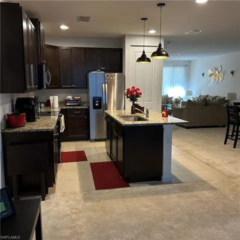 Kitchen featuring light tile patterned floors, light stone countertops, stainless steel appliances, and a sink