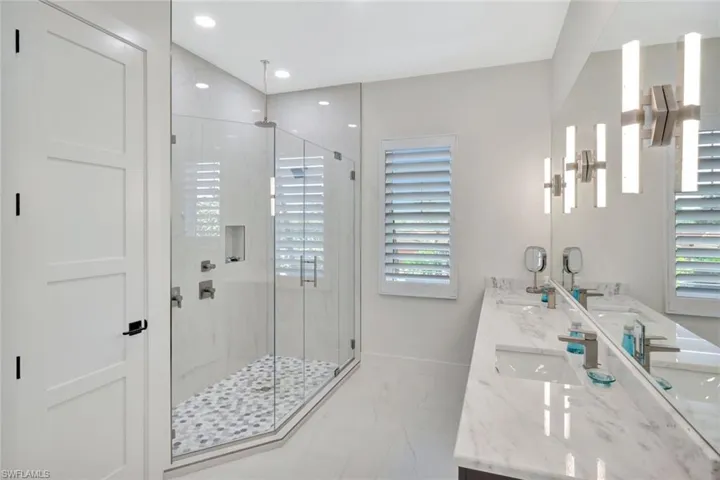 Full bath with a stall shower, double vanity, light marble finish floors, and recessed lighting