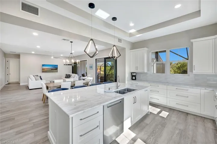 Kitchen featuring white cabinets, light stone counters, open floor plan, dishwasher, and pendant lighting