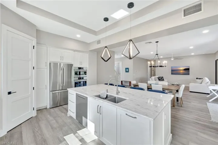 Kitchen featuring open floor plan, decorative light fixtures, white cabinetry, stainless steel appliances, and light stone counters