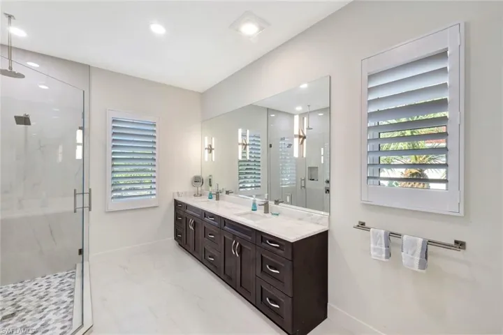 Full bath featuring double vanity, a marble finish shower, and light marble finish flooring