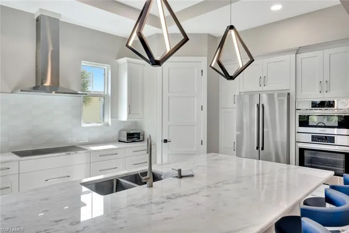 Kitchen with extractor fan, white cabinetry, appliances with stainless steel finishes, and light stone counters