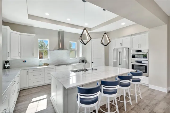 Kitchen featuring white cabinets, stainless steel appliances, a raised ceiling, light stone countertops, and recessed lighting