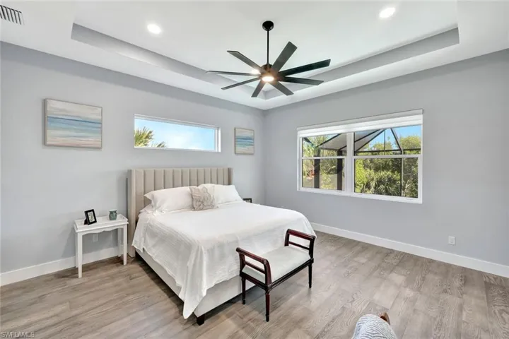 Bedroom featuring a raised ceiling, light wood-type flooring, a ceiling fan, multiple windows, and recessed lighting