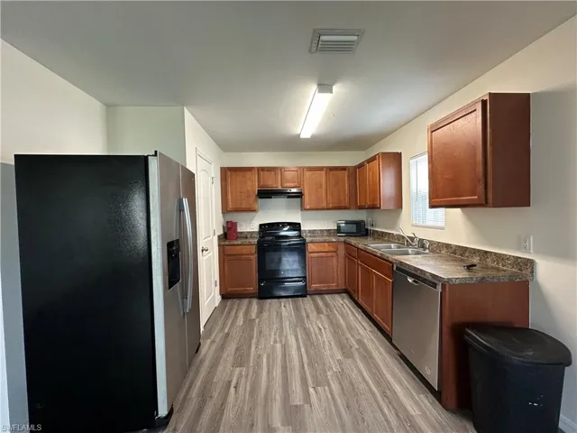 Kitchen with black appliances, dark countertops, brown cabinets, light wood-type flooring, and under cabinet range hood