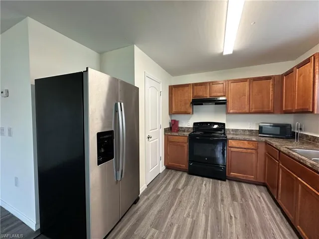 Kitchen with black appliances, brown cabinets, light wood-style flooring, and under cabinet range hood