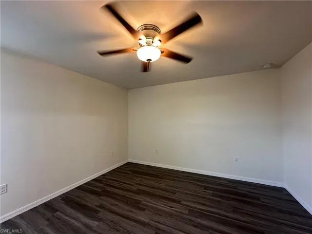 Unfurnished room featuring dark wood-style flooring and a ceiling fan