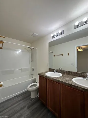 Full bath with double vanity, shower / bath combination, and dark wood-style flooring
