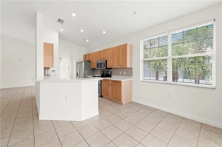 Open concept kitchen featuring recessed lighting, a breakfast bar with a solid surface countertop, light wood cabinetry, and stainless steel appliances