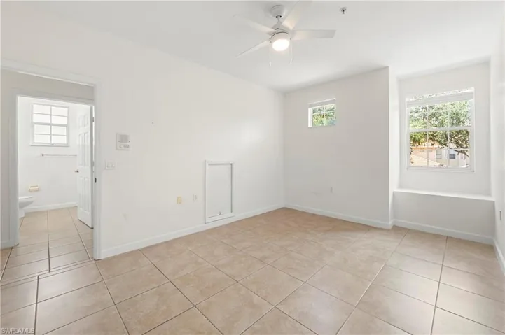 Open concept room featuring neutral tone tile flooring, a ceiling fan with integrated lighting, multiple windows providing natural light, and a built-in window seat