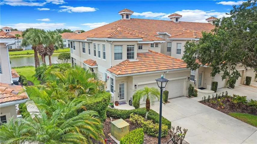 Stucco exterior featuring a terracotta tile roof, attached garage, paved driveway, and established tropical landscaping
