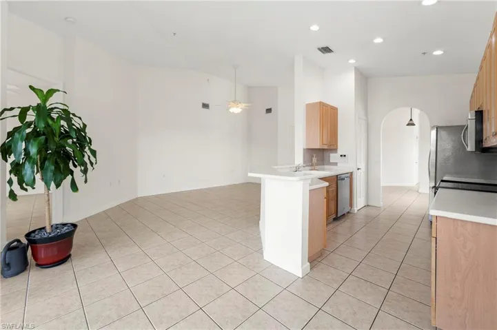 Kitchen and living area featuring tile flooring, light wood-finish cabinetry, stainless steel appliances, and an arched entryway