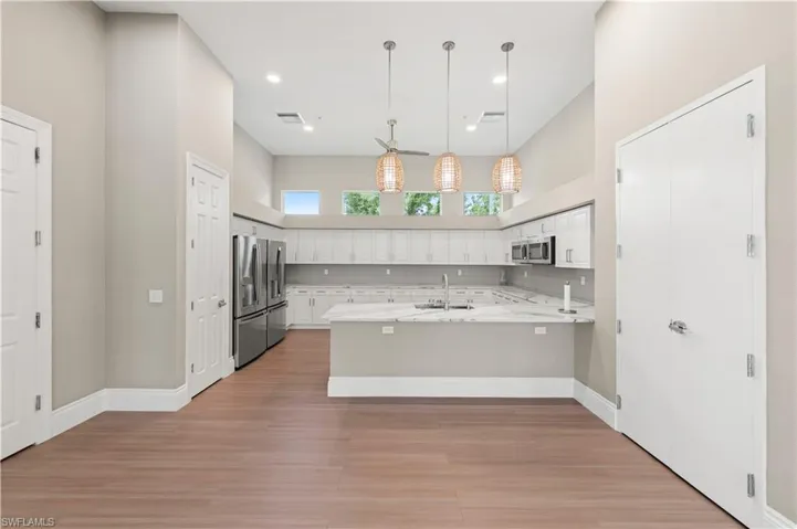 Open-concept kitchen featuring wood-finish flooring, white cabinetry, light countertops, stainless steel appliances, and a vaulted ceiling with pendant lighting