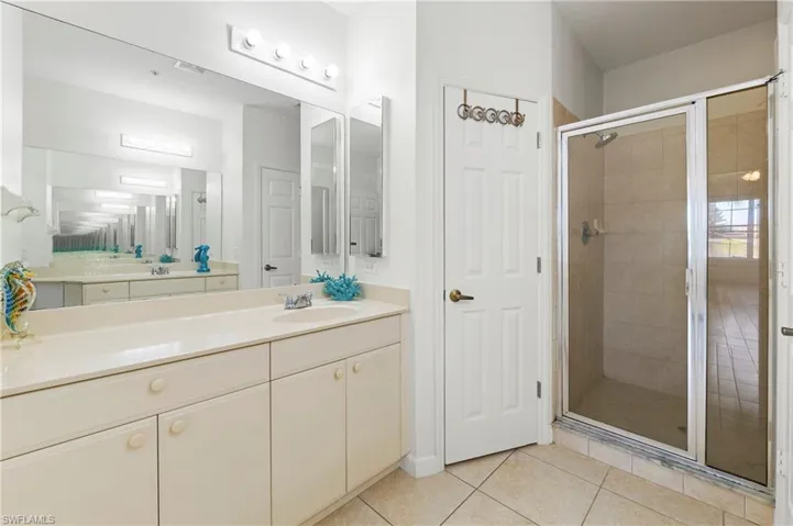 Spacious bathroom featuring a dual vanity with ample counter space, a large wall-mounted mirror, and a glass-enclosed shower with tiled walls