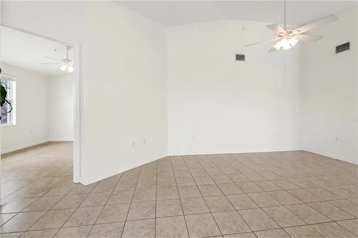 Spacious interior room featuring light-toned tile flooring, vaulted ceilings, and a ceiling fan with integrated lighting