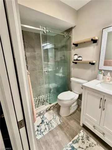 Bathroom with vanity, toilet, wood finished floors, a stall shower, and baseboards