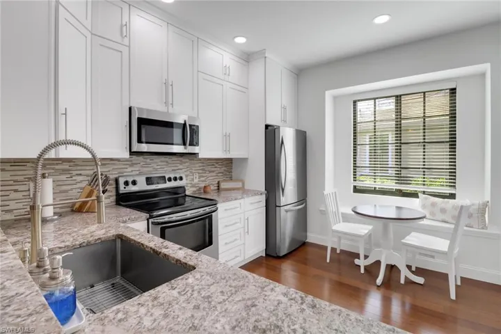 Kitchen with white cabinetry, sink, decorative backsplash, stainless steel appliances, and light stone countertops