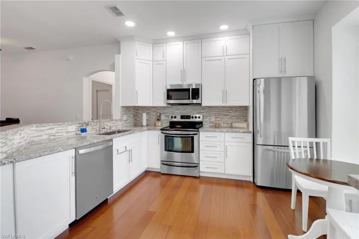Kitchen featuring light stone counters, stainless steel appliances, sink, and white cabinets