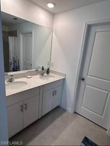 Bathroom featuring double vanity, curtained shower, and light tile patterned flooring