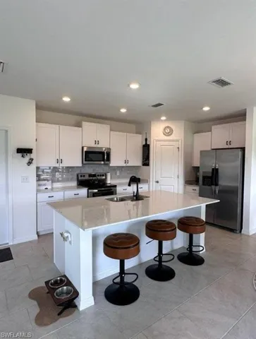 Kitchen featuring a kitchen bar, stainless steel appliances, an island with sink, backsplash, and light stone counters