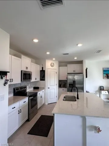 Kitchen featuring stainless steel appliances, light stone countertops, an island with sink, light tile patterned floors, and white cabinets