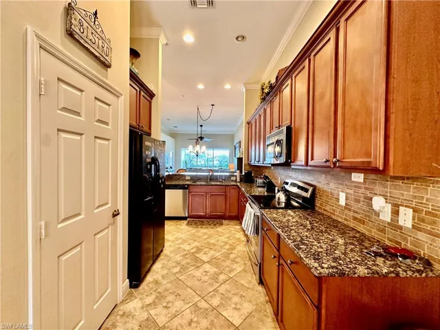 Kitchen featuring dark stone countertops, appliances with stainless steel finishes, light tile patterned flooring, ceiling fan, and ornamental molding