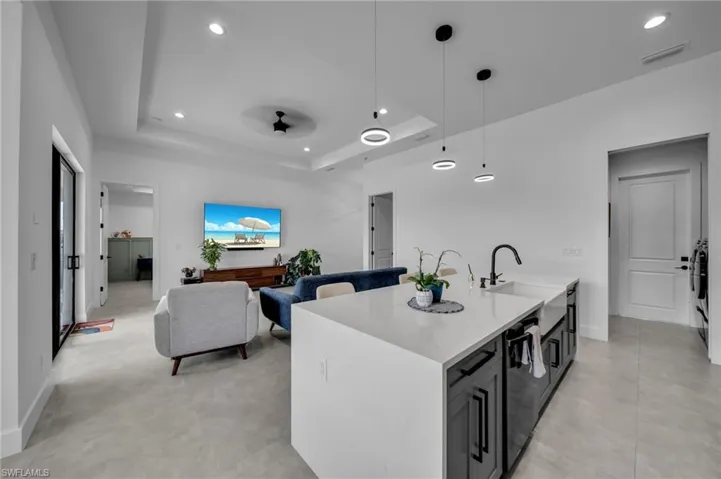 Kitchen with a tray ceiling, recessed lighting, a sink, light countertops, and a center island with sink