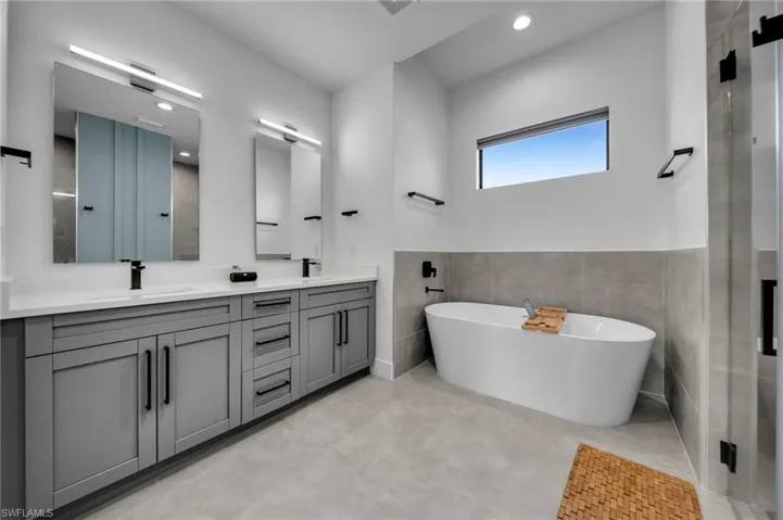 Bathroom with a sink, tile walls, double vanity, and a freestanding tub