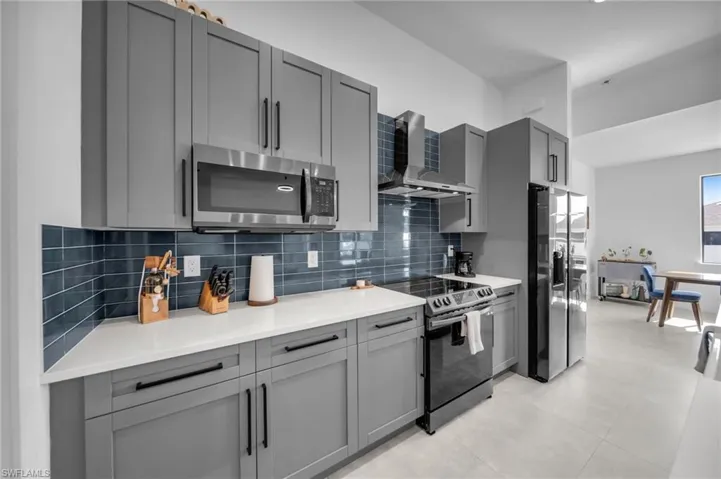 Kitchen featuring wall chimney range hood, gray cabinets, backsplash, and stainless steel appliances