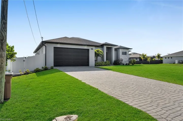 Prairie-style home with stucco siding, decorative driveway, fence, a front lawn, and an attached garage