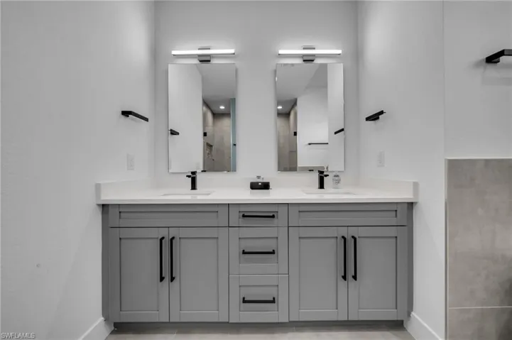 Full bathroom with tiled shower, double vanity, baseboards, and a sink
