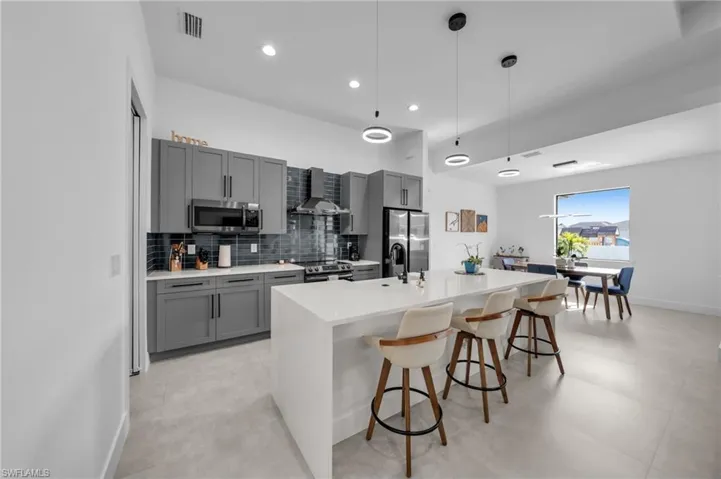 Kitchen with gray cabinets, appliances with stainless steel finishes, wall chimney exhaust hood, and a center island with sink