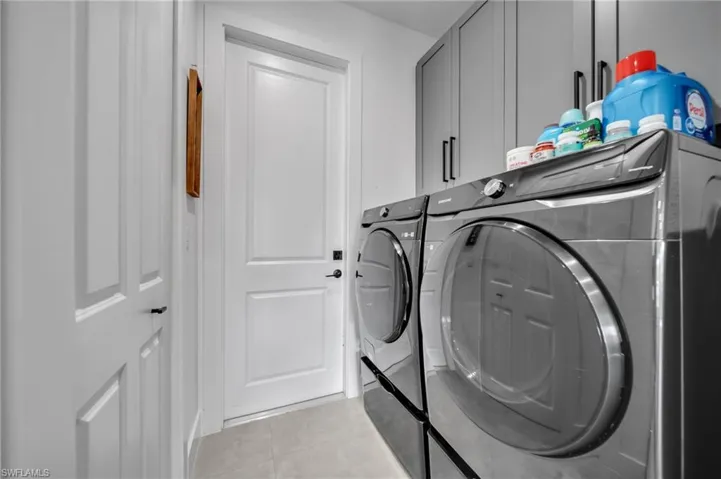 Washroom featuring light tile patterned flooring, cabinet space, and washing machine and dryer