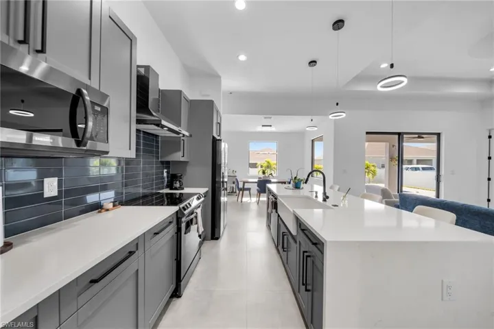 Kitchen with wall chimney exhaust hood, recessed lighting, a sink, stainless steel appliances, and decorative backsplash