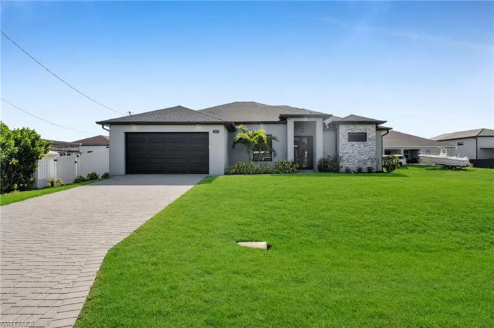 Prairie-style home featuring stucco siding, decorative driveway, a front yard, fence, and an attached garage