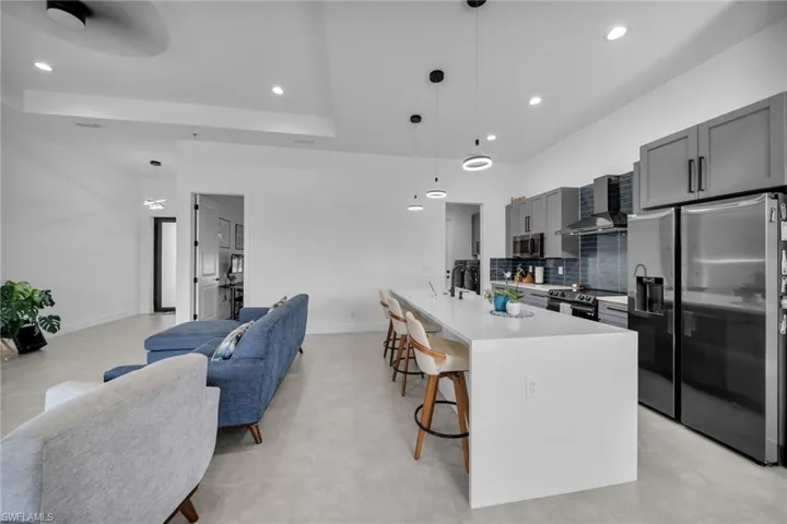 Kitchen featuring wall chimney range hood, open floor plan, light countertops, a kitchen bar, and stainless steel appliances