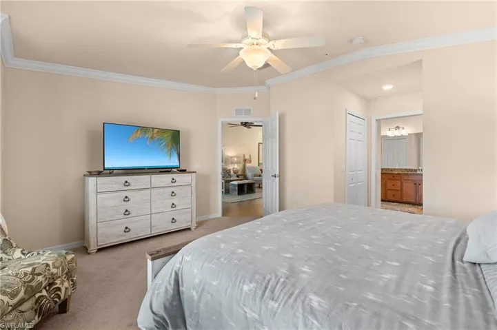 Carpeted bedroom with crown molding, baseboards, ensuite bath, visible vents, and a ceiling fan