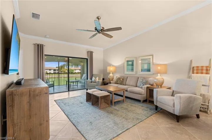 Living area with light tile patterned floors, ornamental molding, visible vents, and a ceiling fan