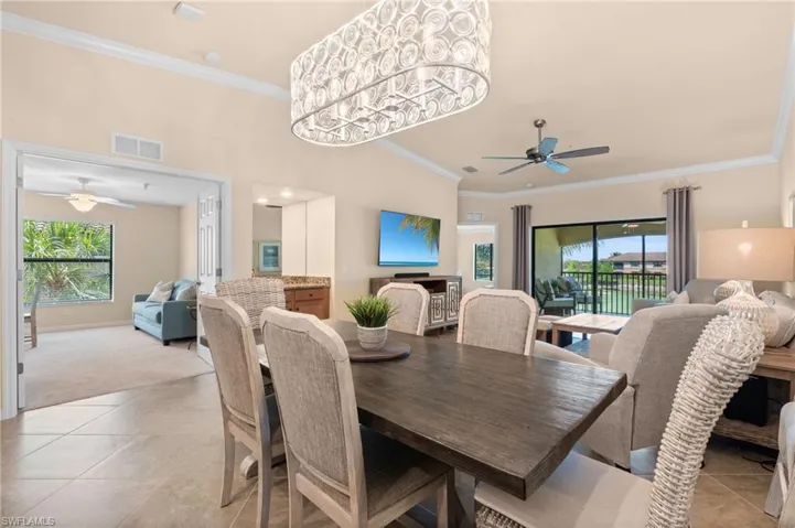 Dining area with light tile patterned floors, ceiling fan with notable chandelier, crown molding, and visible vents