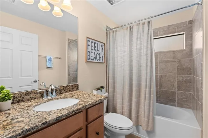 Bathroom featuring toilet, vanity, shower / tub combo, and visible vents