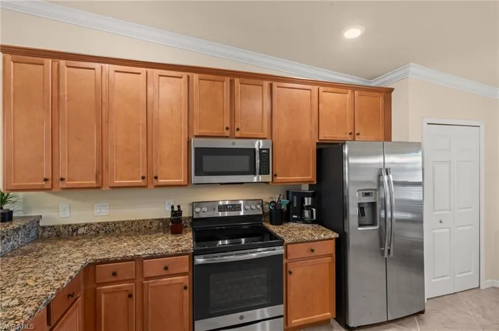 Kitchen featuring brown cabinetry, dark stone countertops, light tile patterned floors, stainless steel appliances, and ornamental molding