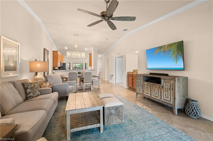Living area featuring vaulted ceiling, light tile patterned floors, ornamental molding, ceiling fan with notable chandelier, and baseboards