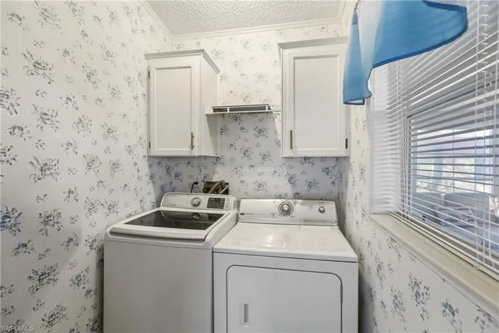 Laundry area with cabinet space, washing machine and clothes dryer, wallpapered walls, and a textured ceiling