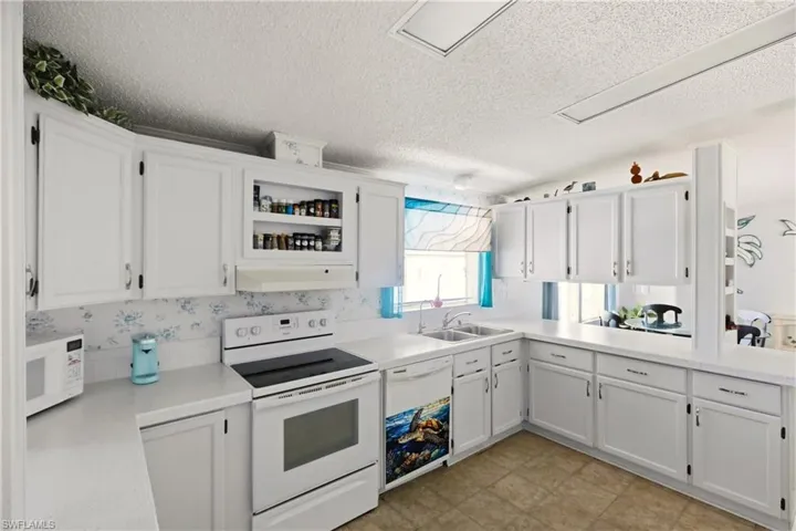 Kitchen featuring white appliances, white cabinetry, light countertops, a textured ceiling, and a peninsula