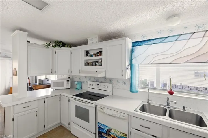 Kitchen featuring white cabinets, white appliances, a textured ceiling, light countertops, and a peninsula